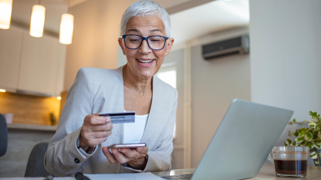 An older woman looking at her credit card while browsing the web