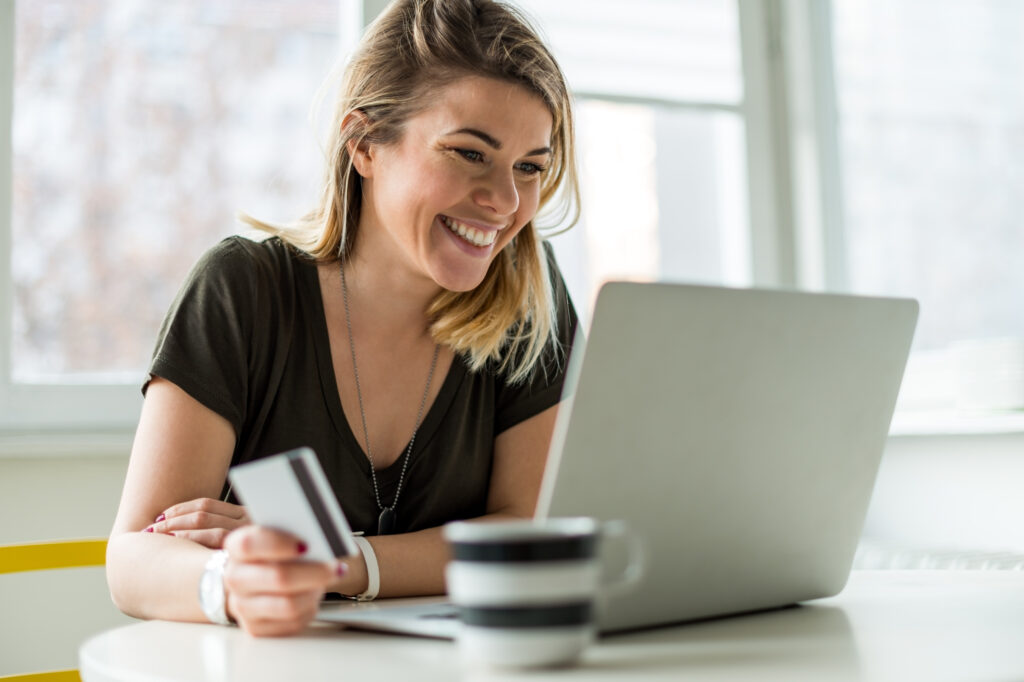 Woman is looking a her laptop while smiling and holding her credit card