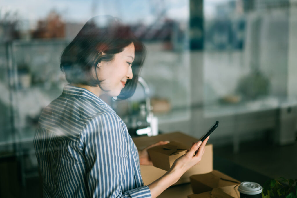 Woman looks at phone while holding a takeout box