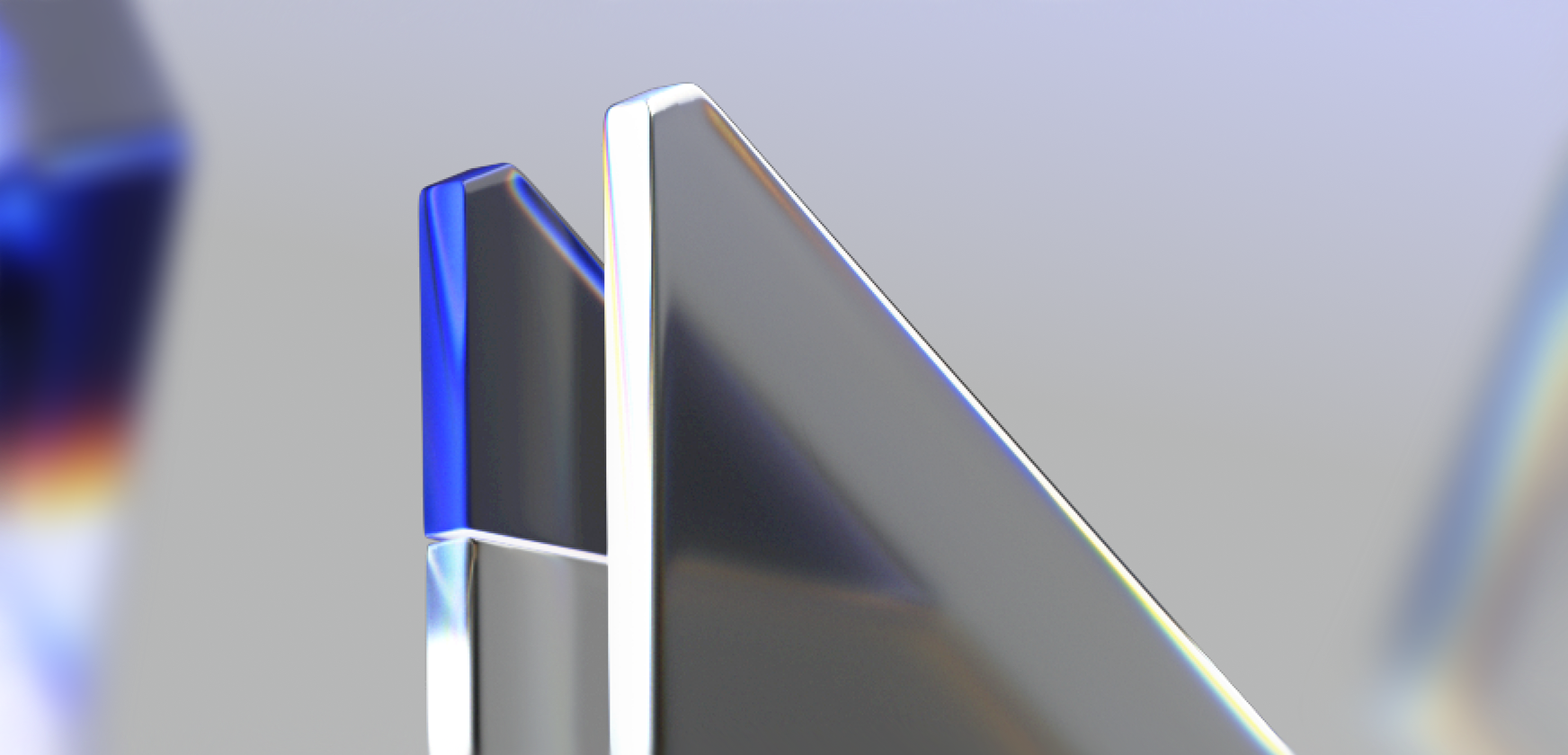 Two abstract, glass-like geometric shapes with sharp edges and reflective surfaces stand upright against a soft, blurred background with hints of blue and purple hues.