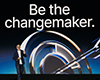 A person stands on stage in front of a large screen displaying the words Be the changemaker above an abstract design.