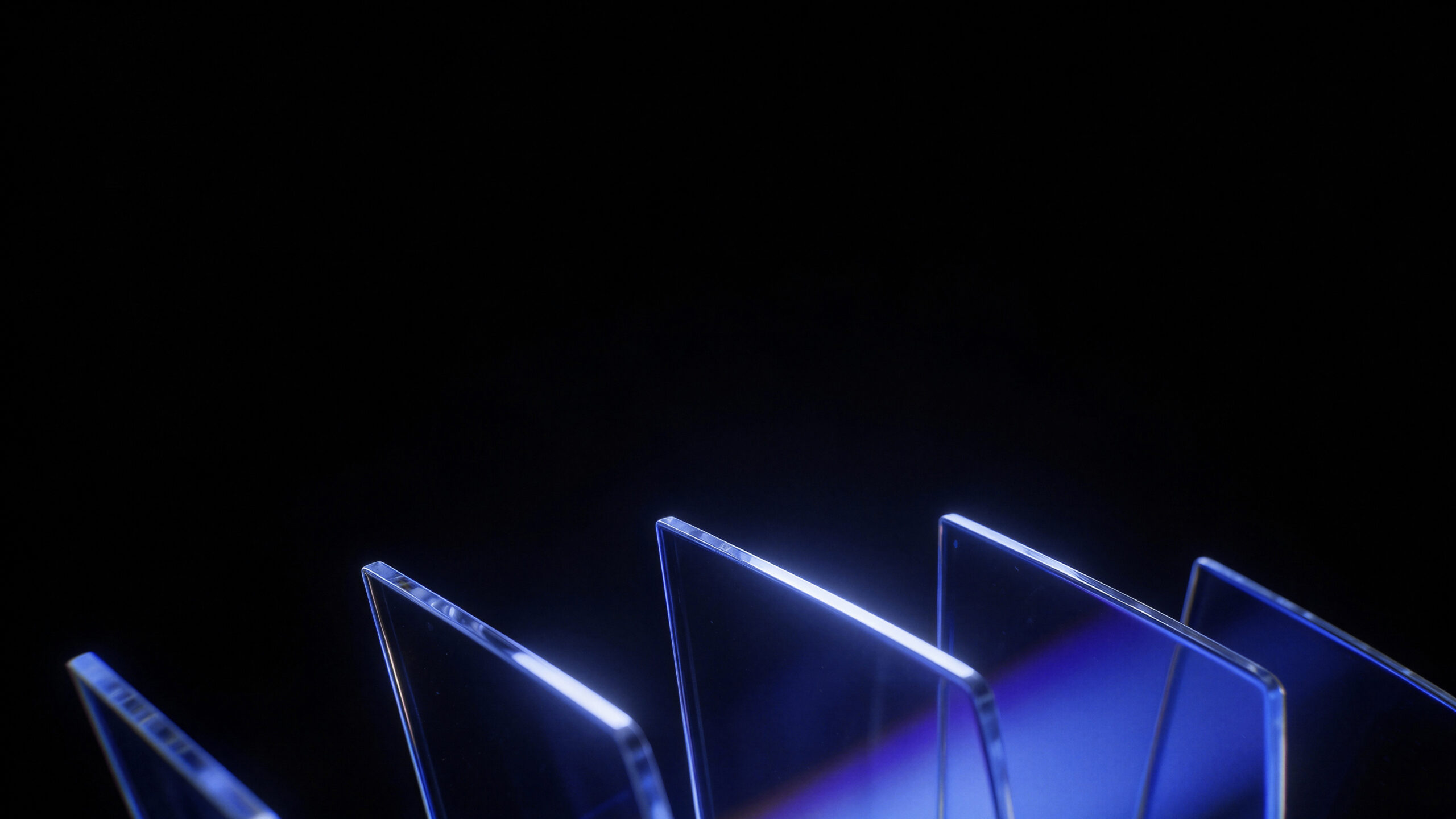 Several transparent glass panels stand upright in a row against a dark background, illuminated by blue light reflecting along their edges.